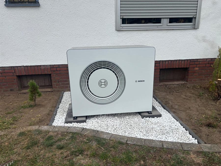 Bosch Luft-Wärmepumpe auf neuem Kiesbett an der Fassade eines Bestandshauses